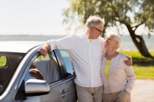 Coppia di anziani in piedi accanto all'auto che si guarda amorevolmente l'un l'altro