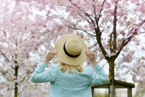 Donna bionda che indossa un cappello mentre si gode gli alberi in fiore di ciliegio