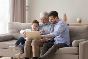 Padre, figlio e nipote seduti su un divano, guardando insieme un laptop mentre sorridono