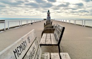 mostra panchine commemorative lungo il centro di una passerella di ingresso con faro alla fine del molo