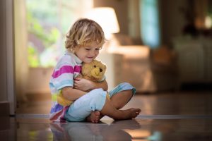 giovane ragazzo seduto a casa abbracciando un orsacchiotto marrone chiaro vicino