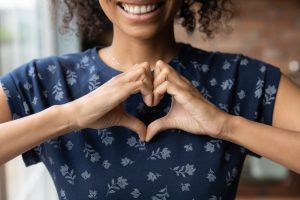 Giovane donna in camicia blu navy che fa un cuore con le mani