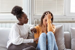 Due giovani amiche sedute su un divano, una triste mentre l'altra offre supporto