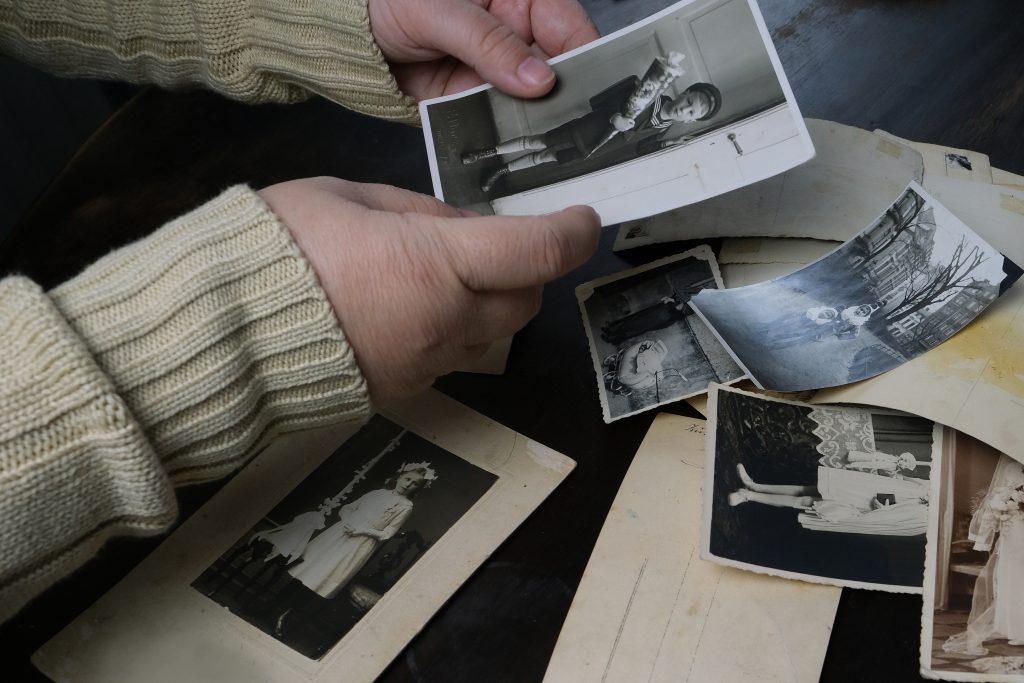 mani femminili che toccano vecchie fotografie degli anni '50, pila di foto sul tavolo, concetto di genealogia, memoria degli antenati, albero genealogico, nostalgia, infanzia, ricordo