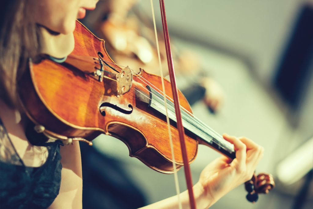 Orchestra sinfonica sul palco, mani che suonano il violino.  Profondità di campo, stile vintage.