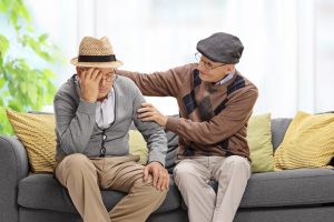 Due uomini anziani seduti su un divano, uno che conforta l'altro che è sconvolto