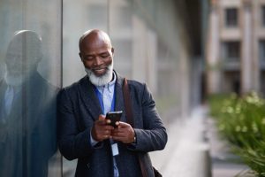 Uomo appoggiato al muro esterno mentre legge i messaggi sul suo cellulare