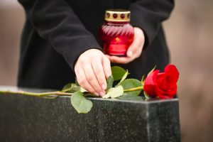 Donna in cappotto nero che lascia una rosa rossa del ricordo su una lapide