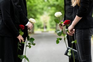 Famiglia di quattro persone vestite di nero, ciascuna con in mano un fiore bianco o rosso del ricordo