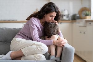 Madre e figlio seduti sul divano di casa, madre che abbraccia il figlio vicino mentre piange ed è sconvolto